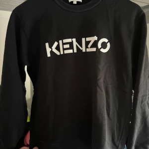 Svart sweatshirt från Kenzo - Säljer en stilren svart sweatshirt från Kenzo med deras ikoniska logga i vitt på framsidan. Tröjan har långa ärmar och en rund halsringning. Perfekt för en avslappnad och trendig look.