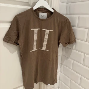 Brun t-shirt från Les Deux - Snygg brun t-shirt från Les Deux med ett stort, broderat 'II' på framsidan. Perfekt för en avslappnad stil. Tillverkad i Turkiet. Defekter på framsida, små hål, bild 3. Nypris: 700kr