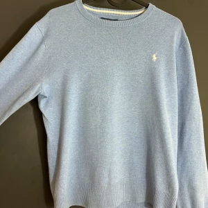 Ralph Lauren tröja Strl Xs - Säljer en stilren ljusblå tröja från Polo Ralph Lauren i mjuk pima bomull. Tröjan har en klassisk rund halsringning och ett diskret broderat logotyp på bröstet. Perfekt för en avslappnad och elegant look. Obs står 14-16 men passar xs