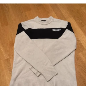 J.Lindeberg tröja - Snygg beige och svart tröja från J.Lindeberg med en broderad logga på bröstet. Tröjan har långa ärmar och ribbade muddar vid ärmslut och nederkant. Hör av dig om du har frågor!