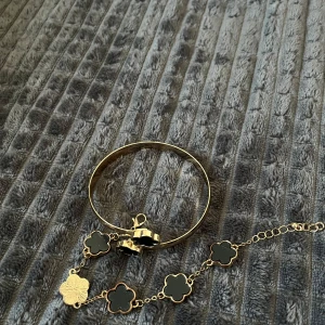 Guldarmband med svartsten  - guldarmband med svarta, klövermotiv. Armbandet har en fast form och ett matchande kedjearmband.