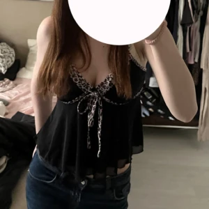 Svart linne med leoparddetaljer - Snyggt svart linne med leopardmönstrade detaljer och knytning framtill. Perfekt för en trendig look. Storlek M men sitter som S. 