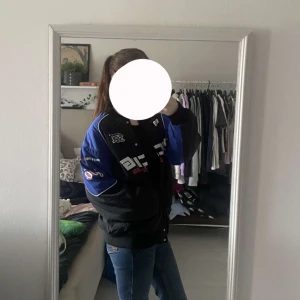 Cool bomberjacka - Säljer en cool racingjacka/bomberjacka i svart och blått med tryck på framsidan och ärmarna. Jackan har en oversize passform och långa ärmar. Perfekt för dig som gillar motorsport och vill ha en stilren look. Storlek S 💙