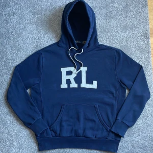 Ralph lauren hoodie - Mörkblå hoodie från Ralph Lauren med vita snören. Hoodien har ett Ralph Lauren märke sytt vid höger ärm. Storlek M.                                      Hör gärna av dig vid frågor eller om du vill ha fler bilder!