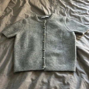 Grå kofta från Zara - Säljer en stilren grå kofta från Zara med korta ärmar och knappar framtill.  Koftan är mjuk och bekväm, idealisk för både vardag och lite finare tillfällen. Skriv till mig om nu har några frågor❤️