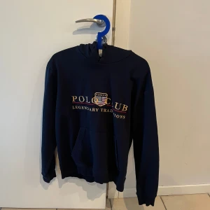 Mörkblå hoodie från Windsor Polo Club - Säljer en snygg mörkblå hoodie från Windsor Polo Club med tryck på framsidan. Tröjan har en klassisk känguruficka och en bekväm huva. Perfekt för en avslappnad stil.