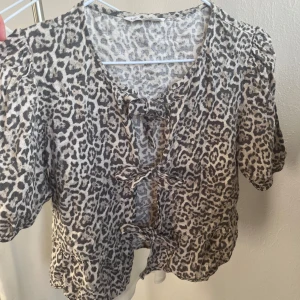 Leopardmönstrad blus - Säljer en leopardmönstrad blus från Stradivarius med korta ärmar och knytning framtill. Perfekt för att piffa upp en outfit. Blusen har en luftig passform och är tillverkad i ett lätt material.