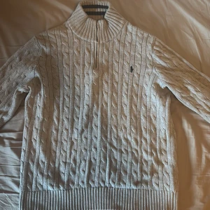 Ljusgrå stickad tröja från Ralph Lauren - Säljer en stilren ljusgrå stickad tröja från Ralph Lauren med stickat mönster. Tröjan har en dragkedja vid halsen och ribbade muddar vid ärmslut och nederkant. Perfekt för lite kyligare dagar! Passar mig perfekt som är 17 år!