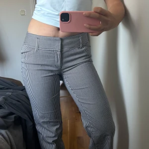 Randiga kostymbyxor med bootcut - Snygga svartvit-randiga kostymbyxor med bootcut passform och normal midja. Byxorna har hällor för bälte, fickor fram och bak samt klassisk stängning med dragkedja och knapp. Perfekta för en stilren look.