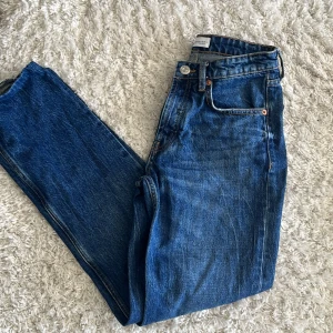 Blå jeansbyxor från Zara - Säljer ett par klassiska blå jeans från Zara med normal passform och raka ben. Byxorna har fem fickor, knappgylf och är tillverkade i ett tåligt jeanstyg. Perfekta till många olika stilar och enkla att matcha.