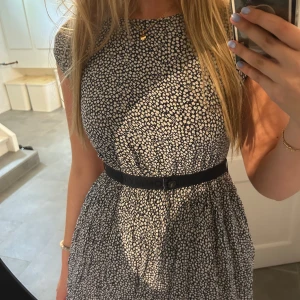 Blommig klänning från Tommy Hilfiger - Såå söt blommig klänning från Tommy Hilfiger!! Den har ett blommigt mönster i vitt och mörkblå/svart. Den har ett bälte i midjan som verkligen framhäver figuren. Storleken är ”164 cm”. Kortärmad och kjolen har lager av tyg. Säljer då den är för liten 