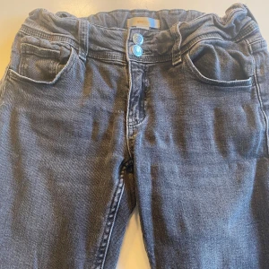 Grå jeansbyxor från Gina Tricot - Snygga grå jeansbyxor från Gina Tricot med raka ben och dubbla knappar i midjan. Klassisk femficksmodell med ficklock och knapp bak. Perfekta för en avslappnad stil.