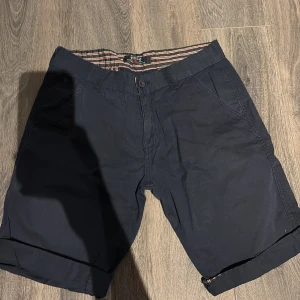 Mörkblå shorts från Polo Ralph Lauren - Snygga mörkblå shorts från Polo Ralph Lauren med klassisk passform. Shortsen har fickor fram och bak, knäppning med knapp och dragkedja samt randigt innerfoder i midjan. Perfekta för sommardagar.