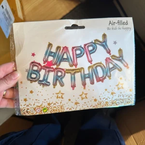 Happy Birthday ballongbokstäver ballonger  - Säljer ett paket med färgglada folieballonger som bildar texten 'HAPPY BIRTHDAY'. Ballongerna är luftfyllda och har en glansig yta i guld, rosa och blått. Perfekt dekoration till födelsedagsfirande. Förpackningen har stjärnmönster och instruktioner på engelska.