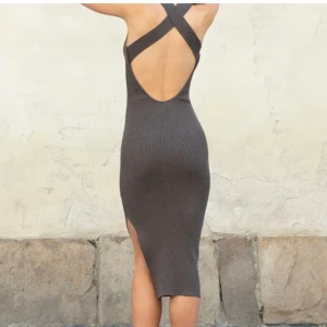 Brun ribbad långklänning med öppen rygg - Säljer en brun, tight ribbad långklänning med snygg öppen rygg och korsade axelband. Klänningen har hög halsringning och en slits framtill för extra stilpoäng. 