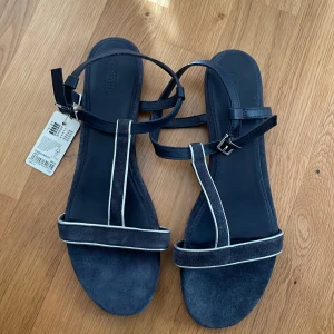 Mörk blå sandaler från Esprit med silver detaljer - Säljer ett par mörk blå sandaler från Esprit med silver kontrastdetaljer. De har en smal rem över tårna och en justerbar rem runt vristen med spänne. Perfekta för varma dagar och enkel stil.