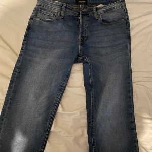 Blå jeans Tapered/Mike jack and jones - Säljer ett par klassiska blå jeans i modellen Tapered/Mike med normal passform och avsmalnande ben. Jeansen har fem fickor, dragkedja och knapp i gylfen samt snygga slitningar framtill. Midjemått W30.