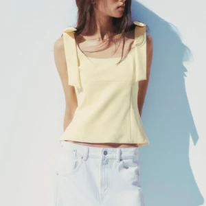 Gul topp med rosetter Zara xs - Söt ljusgul linnetopp med breda axelband och rosetter på axlarna. Toppen har en fyrkantig urringning och är figursydd för en feminin siluett. Perfekt för varma dagar och enkel att matcha med jeans eller kjol.