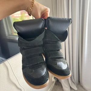 Svarta sneakers med kilklack från Isabel Marant - Skulle säga dem är små i storleken då jag har storlek 39 och dem perfekt på mig🫶🏽 Säljer ett par svarta sneakers med kilklack från Isabel Marant. Skorna har kardborreband, rund tå och en gummisula i beige. Tillverkade i mocka och skinn med cool, sportig design och högt skaft. 