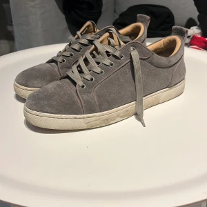  Christian Louboutin med kvitto (real) - Gråa sneakers i mocka från Christian Louboutin med klassisk röd sula. Skorna har snörning och rund tå, samt en vit platt sula. Insidan är beige och de har en stilren och enkel design som passar till många outfits.