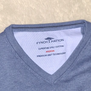 Blå v-ringad tröja från Fynch Hatton - Säljer en stilren blå v-ringad tröja från Fynch Hatton i mjuk bomull. Tröjan har långa ärmar och diskret logga broderad på bröstet. Perfekt för en avslappnad men snygg look.