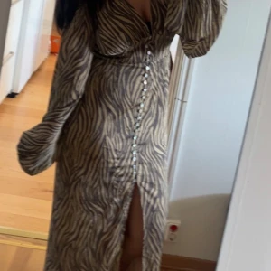 Zebramönstrad långklänning med knappar - Säljer en långklänning med zebramönster och djup v-ringning. Klänningen har långa puffärmar, markerad midja och knappar framtill samt en slits. 💗den är liten i storleken så skulle säga att den passar dig som har storlek 38 