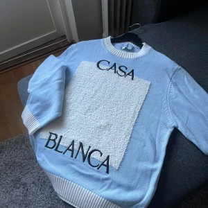 Ljusblå stickad tröja från Casablanca - Säljer en ljusblå stickad tröja från Casablanca med vit panel framtill och svart text 'CASA BLANCA'. Tröjan har rund halsringning och långa ärmar. Ribbstickade muddar vid ärmslut och nederkant. Den är helt ny egentligen. Jag har aldrig använt den då den är lite för stor för mig. 