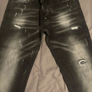 Svarta slitna jeans från Dsquared2 - Säljer ett par svarta jeans från Dsquared2 med slitningar och blekta detaljer. Jeansen har klassisk femficksmodell och dragkedja i gylfen. Snygg streetstil med distressed look. Aldrig använt.