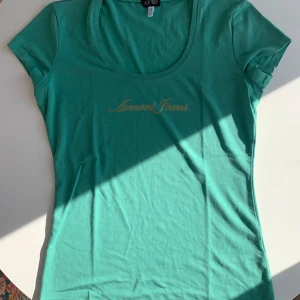 Vintage Armani Tee | Unik Georgio Armani  - Unik Snygg Vintage Tee från Armani. Den har  guldig broderad loga. Lyxigt material och märks att det är hög kvalitet. Har inga tecken på användning. Snygg att ha även bakochfram så att urringningen är i ryggen. Bara att skriva för fler bilder! Passar lite löst i midjan på mig som har S och är mer fitted/tajt för dig som har M-L