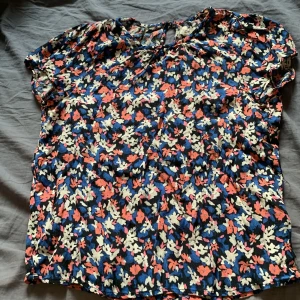 Blommig blus från Lindex - Säljer en blommig blus från Lindex i viskosblandning. Blusen har korta ärmar och ett färgglatt mönster i blått, vitt, rosa och orange. Perfekt för dig som gillar färg och mönster!