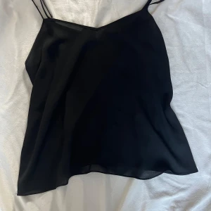 Svart fest topp med tunna axelband - Säljer en svart fest eller BASIC topp med tunna axelband och v-ringning. Toppen är luftig och har en enkel, stilren design som passar perfekt till sommaren. Materialet känns lätt och svalt mot huden.Skriv privat för fler bilder eller andra frågor 💞 