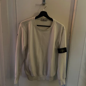 Vit sweatshirt från Stone Island - Hej, jag säljer en stilren vit sweatshirt från Stone Island men den ikoniska loggan på vänster ärm. Tröjan är väldigt bekväm och perfekt för en clean och avslappnad look. Pris kan diskuteras!