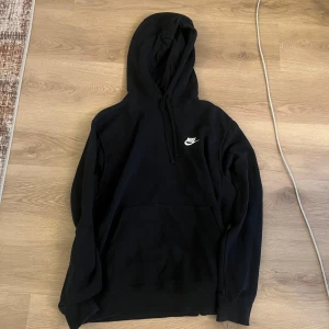 Svart hoodie från Nike - Klassisk svart hoodie från Nike med vit logga på bröstet. Tröjan har huva med dragsko och en stor magficka framtill. Perfekt för en avslappnad stil.