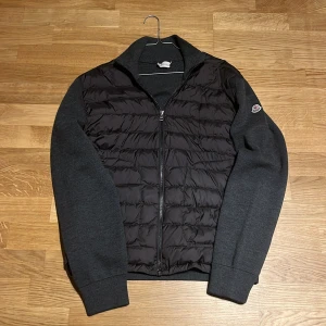 Moncler cardigan  - Säljer en tvärfet Moncler cardigan i färgen grå. Den är köpt på NK för några år sen av min styvfarsa men han har nästan aldrig använt den. Skicket är 9/10 Det är storlek L typ men det står XXL. Skannen funkar även om den är lite gammal. Nytt pris är cirka 11 000. Hör av er vid eventuella funderingar och pris är ej hugget i sten 🪨 