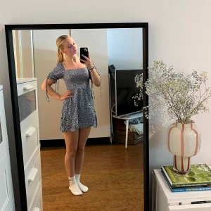 Blå blommig klänning med puffärm - Blå kortklänning med vita små blommor, puffärmar med knytband och smockad överdel. Klänningen har fyrkantig ringning som också går att ha som off-shoulder. Lätt och flowy känsla, säljer då den är för kort för min smak och då inte kommit till användning. (Liten i storleken på längden)