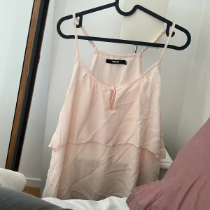 Ljusrosa linnetopp från BikBok - Supersöt ljusrosa linnetopp från BikBok med tunna axelband och dubbla lager tyg som ger en flowy känsla. Toppen har en liten öppning framtill med knyt.
