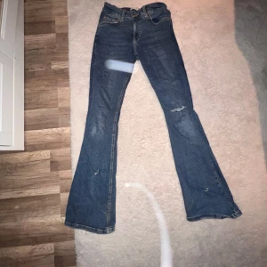 Blå bootcut jeans från Perfect Jeans - Säljer ett par klassiska blå bootcut jeans från Gina tricot i storlek 36. Jeansen har en snygg utsvängd passform,  slitna detaljer på benen för en cool look. Perfekta till sneakers eller boots.