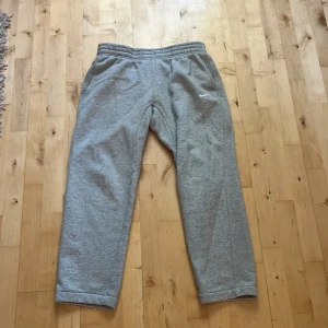 Grå mjukisbyxor från Nike, storlek L - Snygga grå mjukisbyxor från Nike i storlek L. Byxorna har elastisk midja, sidofickor och en bakficka. Perfekta för chill eller träning, med klassisk Nike-logga på benet. Mjukt material som känns skönt mot huden. Passar folk mellan 169-180