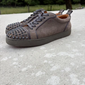 Christian Louboutin sneakers med nitar - Gråbruna sneakers i mocka från Christian Louboutin med ikonisk röd sula och coola svarta nitar på tån. Skorna har snörning och platt sula, perfekt för dig som vill sticka ut med en edgy streetstil. Priset kan diskuteras . Se defekter ( bild 4 och 5 ). OBS samma skor som min andra annons 