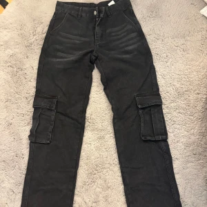 Svarta cargopants med fickor - Svarta cargopants med stora sidofickor och raka ben. Byxorna har klassisk cargostil med flera fickor och är tillverkade i ett jeansliknande material. Perfekta för en avslappnad och cool streetlook.