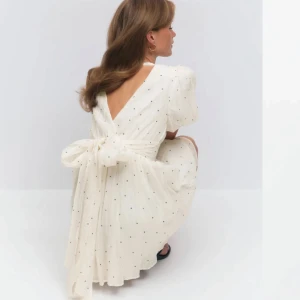 Vit kortklänning med rosett och puffärm - Supersöt vit kortklänning med små svarta prickar, puffiga kortärmar och djup v-ringning. Klänningen har en stor rosett i ryggen! HELT SLUTSÅLD!!! Prislappar kvar 