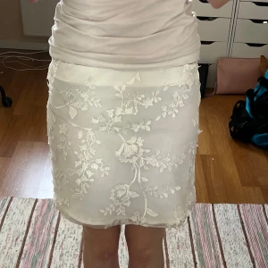 Vit blommig kjol  - Superfin vit kortkjol från BikBok med broderade blommor och transparent lager ovanpå. Kjolen har en rak passform och är perfekt för dig som gillar romantiska detaljer och ljusa färger.
