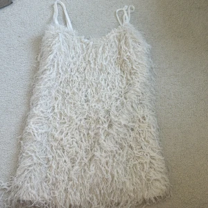 Fluffig vit kortklänning med smala band - Supersöt kortklänning i vitt med fluffig, pälsliknande textur och smala axelband. Klänningen har en unik look med sitt lurviga material och passar perfekt för dig som vill sticka ut. Perfekt för sommarens alla tillfällen!