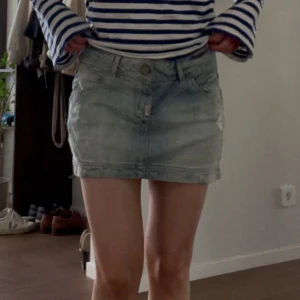 Ljusblå jeanskjol från Pull&Bear - Säljer en ljusblå jeanskjol från Pull&Bear med slitna detaljer och klassiska fickor både fram och bak. Kjolen är kort och har bälteshällor, knapp och dragkedja framtill. 