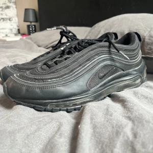 Air Max 97 - Säljer ett par snygga Nike Air Max 97 i svart färg med klassiska reflekterande detaljer som syns extra tydligt i blixt eller starkt ljus. Skorna är använda men i mycket gott skick. de är väl omhändertagna och har använts sparsamt. Sulan är hel, luften i sulan är intakt och ovandelen har bara små tecken på normalt bruk. Storlek 43 men passar även 42/5. Priset går att diskuteras 