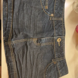 Mörkblå jeanskjol med fickor - Snygg mörkblå jeanskjol med kontrastsömmar och klassiska fickor både fram och bak. Kjolen har bälteshällor och knäppning framtill. Perfekt för dig som gillar en enkel men cool stil.