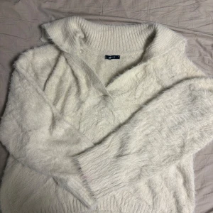 Vit fluffig stickad tröja från Gina Tricot - Supermjuk och fluffig vit stickad tröja från Gina Tricot med bred krage och v-ringning. Tröjan har lång ärm och ribbade muddar vid ärmslut och nederkant. Perfekt för lager-på-lager och en mysig look.