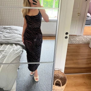 Brun zebramönstrad långklänning NAKD - Supersnygg långklänning från NAKD i brun och svart zebramönster. Klänningen har smala axelband, öppen rygg med snörning och en figurnära passform. Materialet är mjukt och följsamt. Aldrig använd