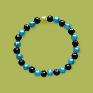 Färgglatt pärlarmband i blått och svart - Snyggt armband med runda pärlor i turkosblått, svart och en gul detalj. Pärlorna är glansiga och sitter på en elastisk tråd, vilket gör det enkelt att ta på och av. Liten I storleken 