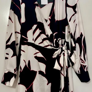Mönstrad omlottklänning med knyt - Snygg omlottklänning med svart och vit bas, stora abstrakta mönster och röda detaljer. Klänningen har långa ärmar och knyt i midjan för en cool och trendig look. Perfekt för dig som gillar statement-plagg och vill sticka ut.